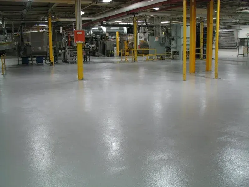Empty industrial warehouse with polished gray floor, yellow columns, and machinery in the background