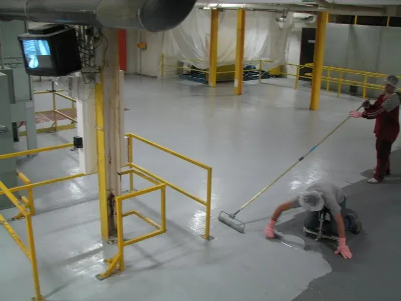 Industrial floor cleaning crew mopping a shiny warehouse floor near yellow railings and pipes