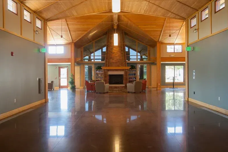Spacious empty hall with a wooden vaulted ceiling, stone fireplace, and glossy polished floor.