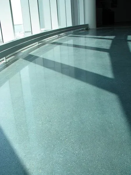 Sunlit empty corridor with large windows and long shadows across a glossy floor