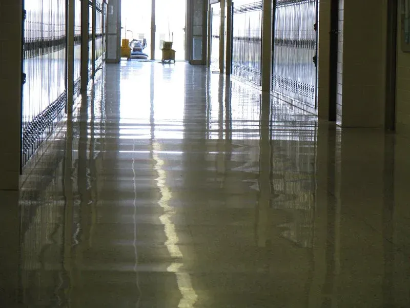Empty hallway with a glossy reflective floor and barred windows along both sides