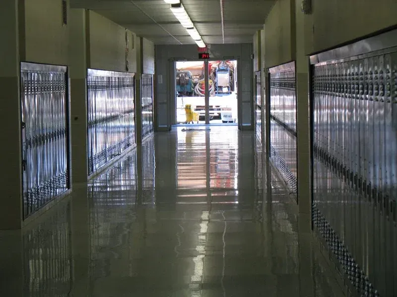 Empty school hallway with green lockers and a shiny tiled floor leading to an open doorway