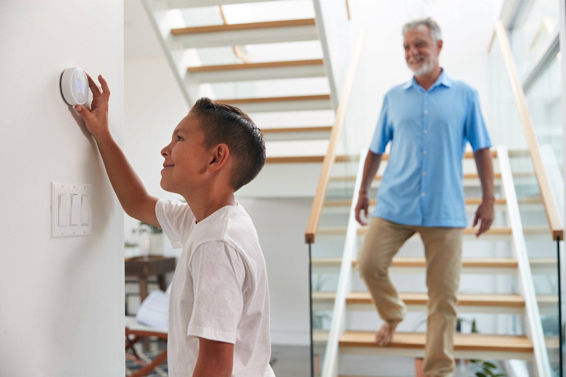 Un garçon règle un thermostat tandis qu'un homme plus âgé descend les escaliers.