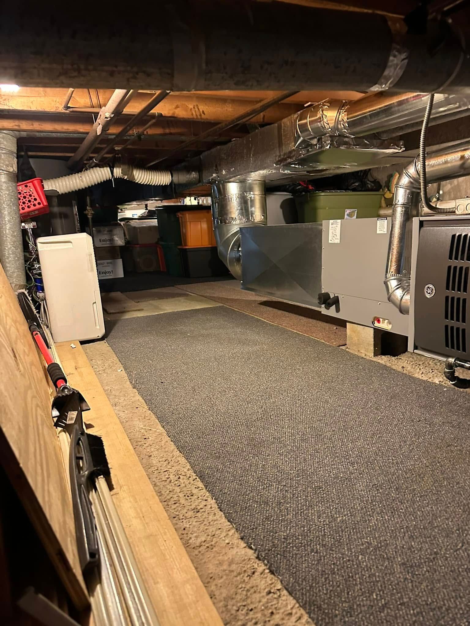A crawl space featuring a gravel floor, exposed wooden beams, HVAC equipment, and several storage containers.
