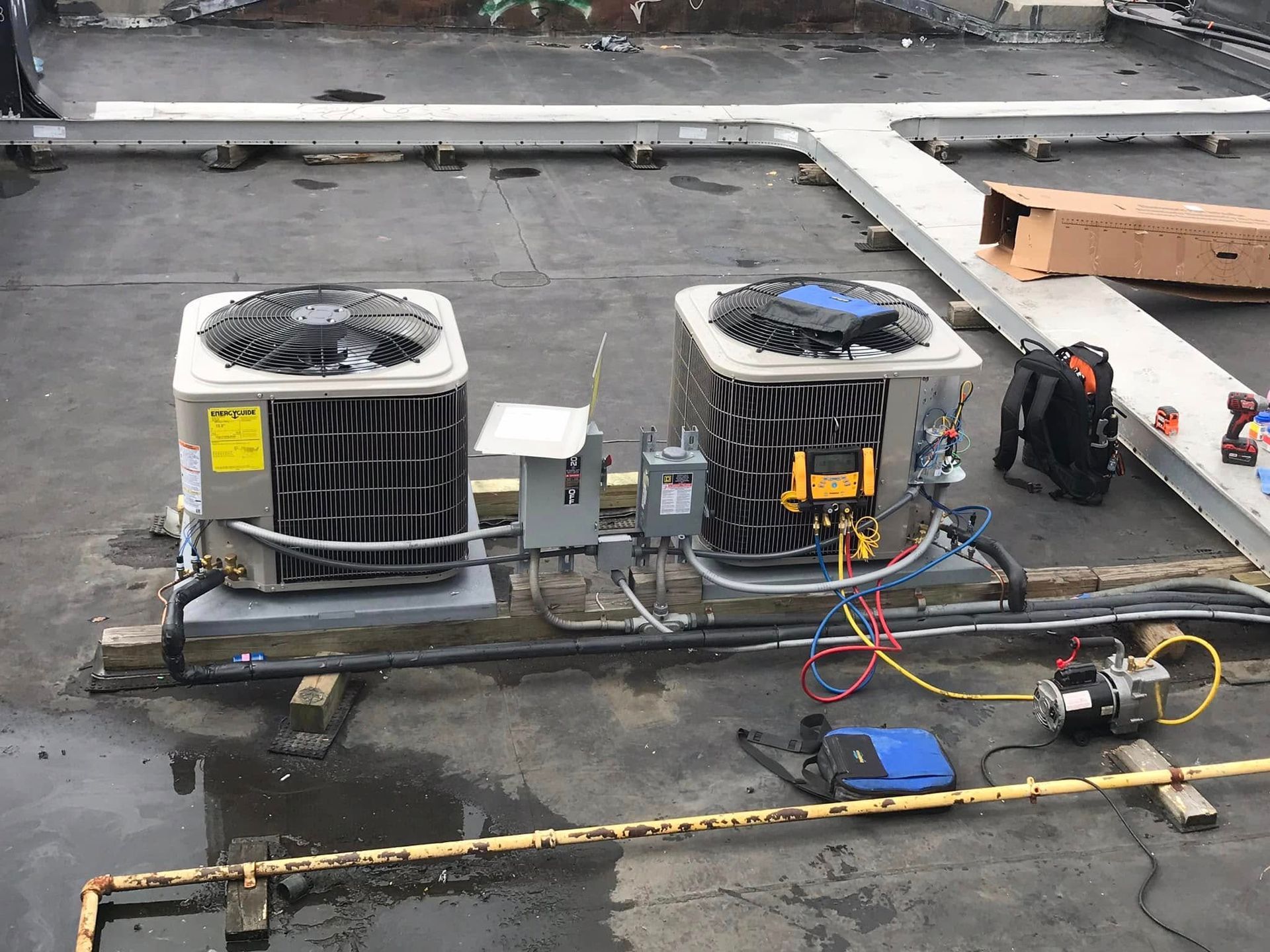 Two HVAC condenser units on a rooftop with gauges, a vacuum pump, and tools used for professional maintenance.