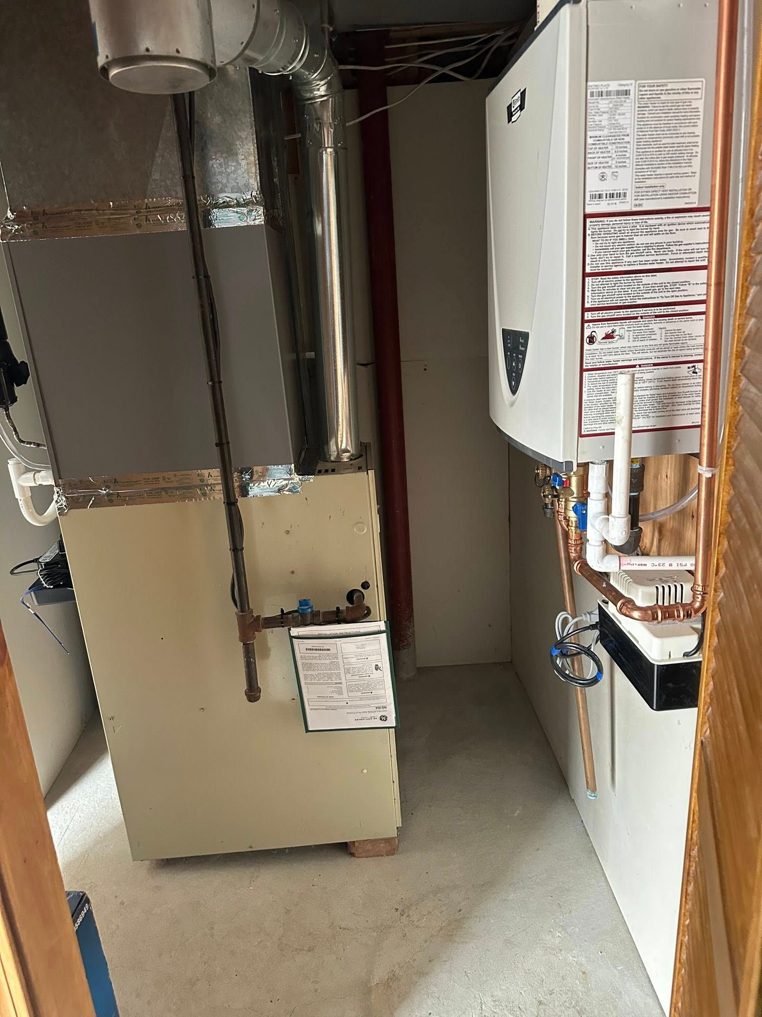 A utility room featuring a furnace with silver ductwork on the left and a wall-mounted boiler unit on the right.