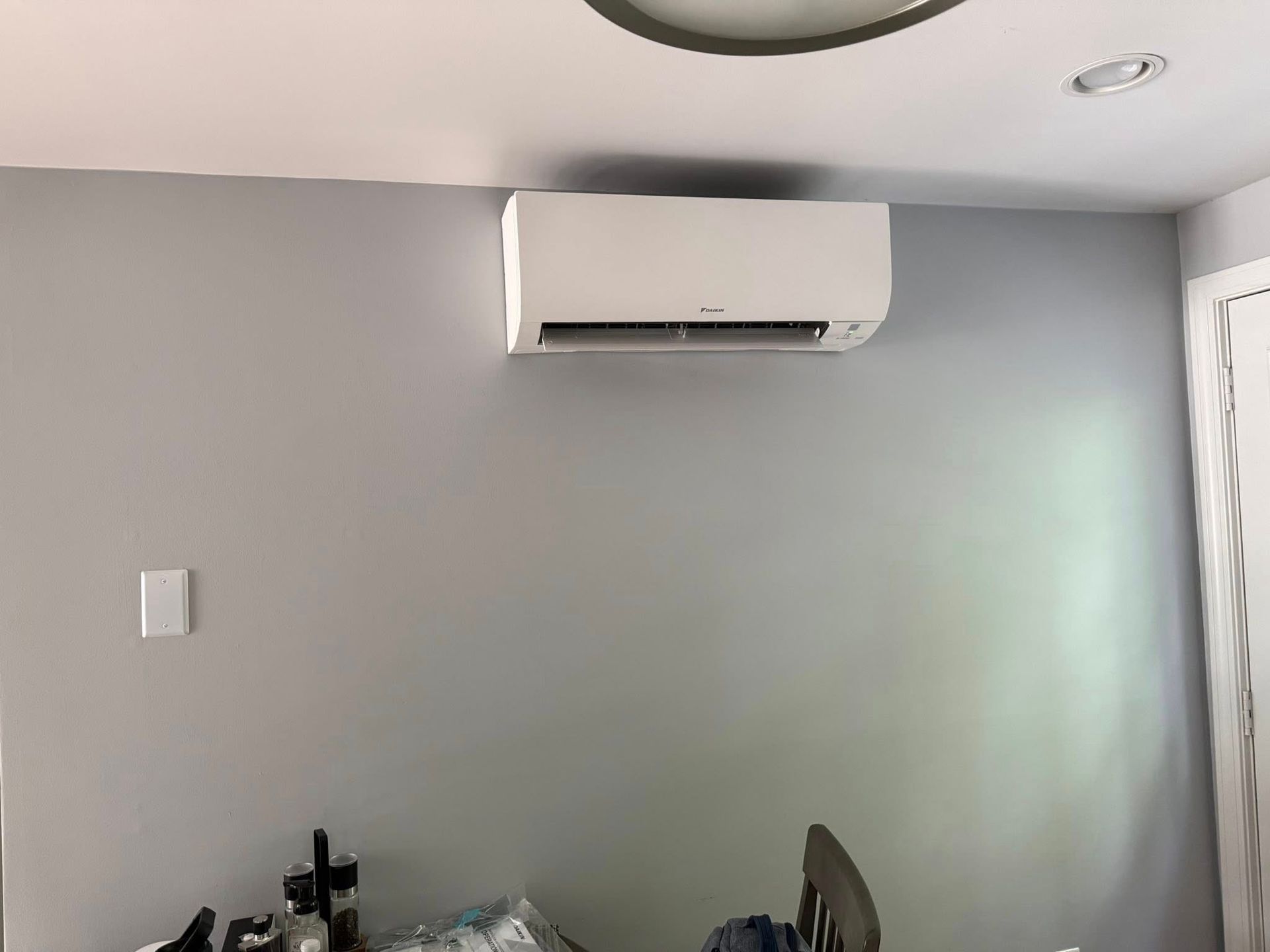 A white wall-mounted air conditioner unit centered on a plain light grey wall in a room.
