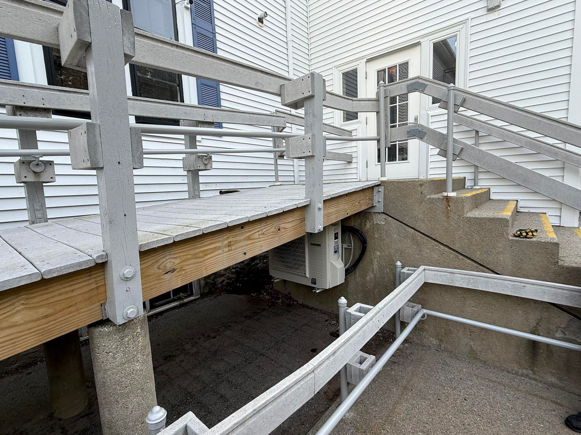 A wooden wheelchair ramp and adjacent concrete stairs leading to the entrance of a white building.