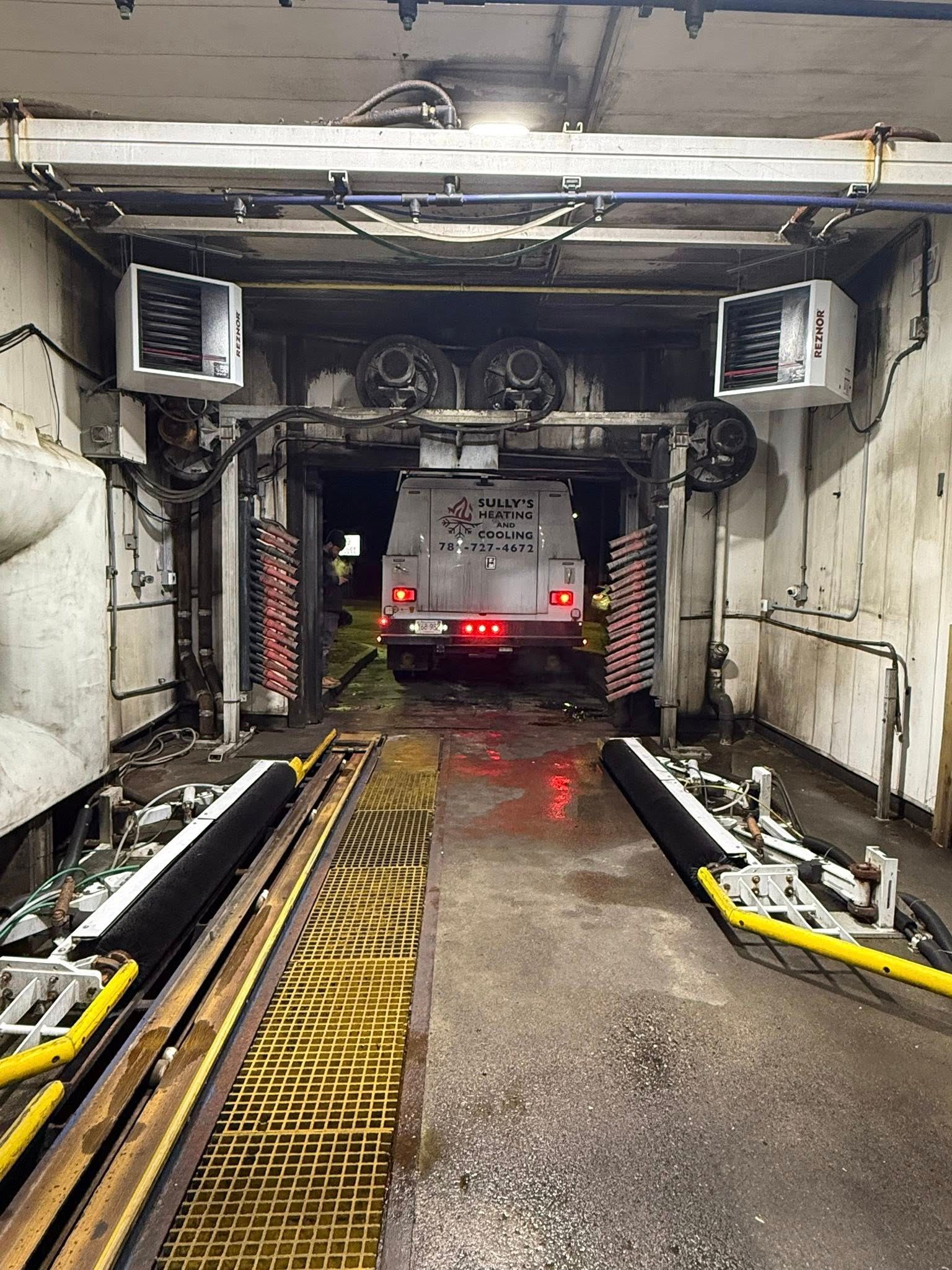 A white service truck is positioned inside a commercial car wash tunnel with cleaning equipment on both sides.