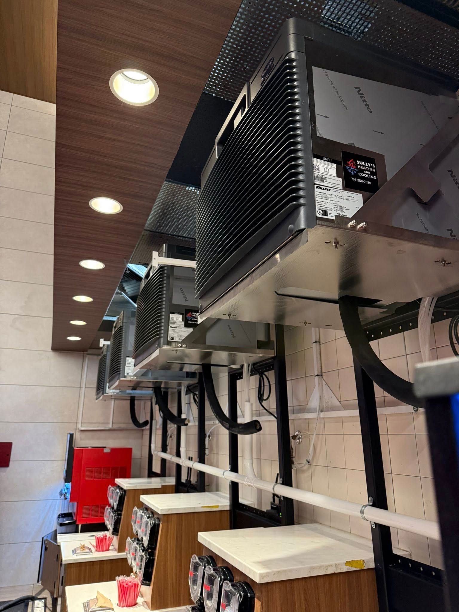 A row of industrial-style food warmers mounted above service counters in a brightly lit, modern commercial kitchen space.