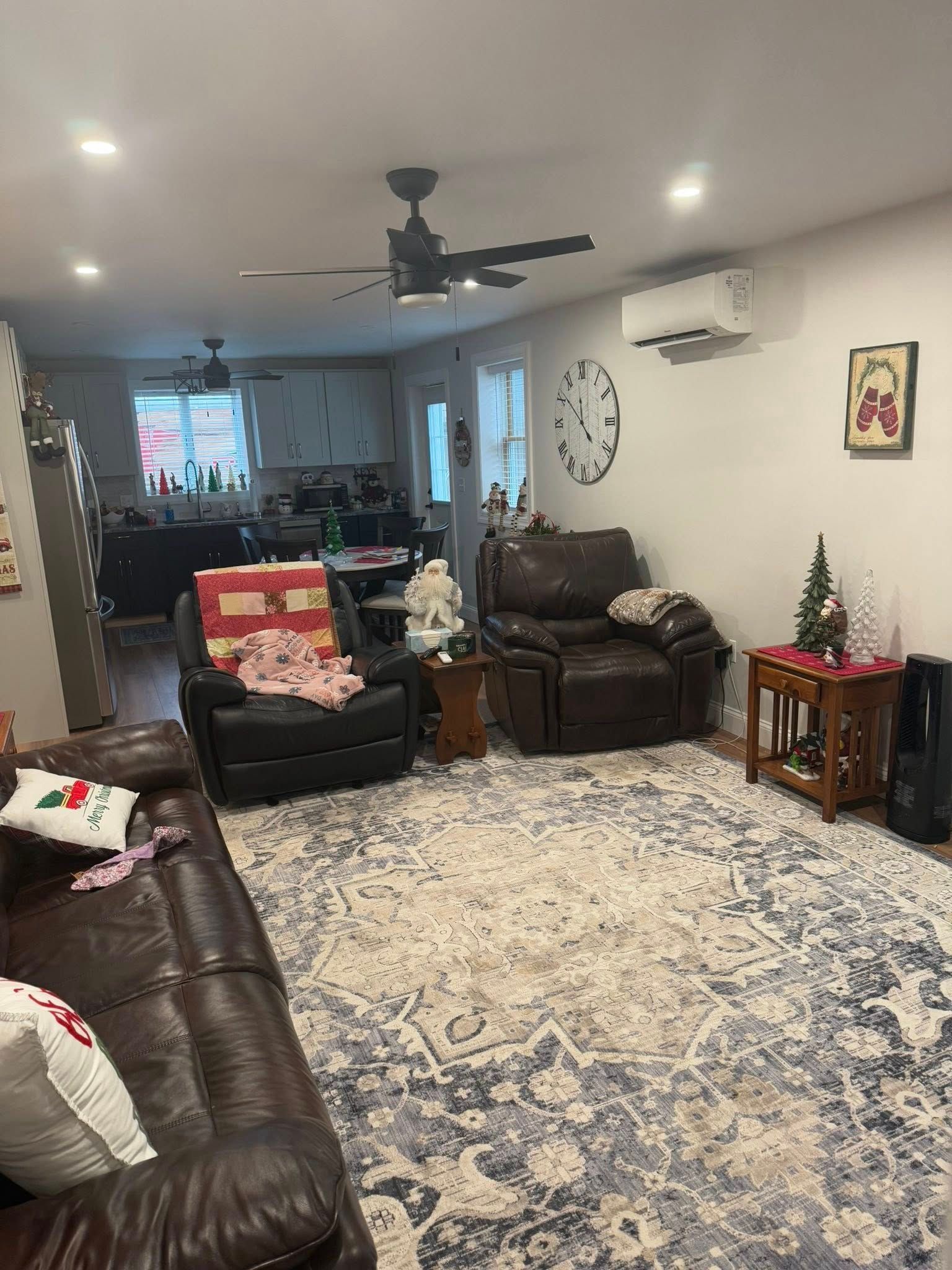 Living room with dark leather furniture, a large blue and white patterned rug, and holiday decorations.
