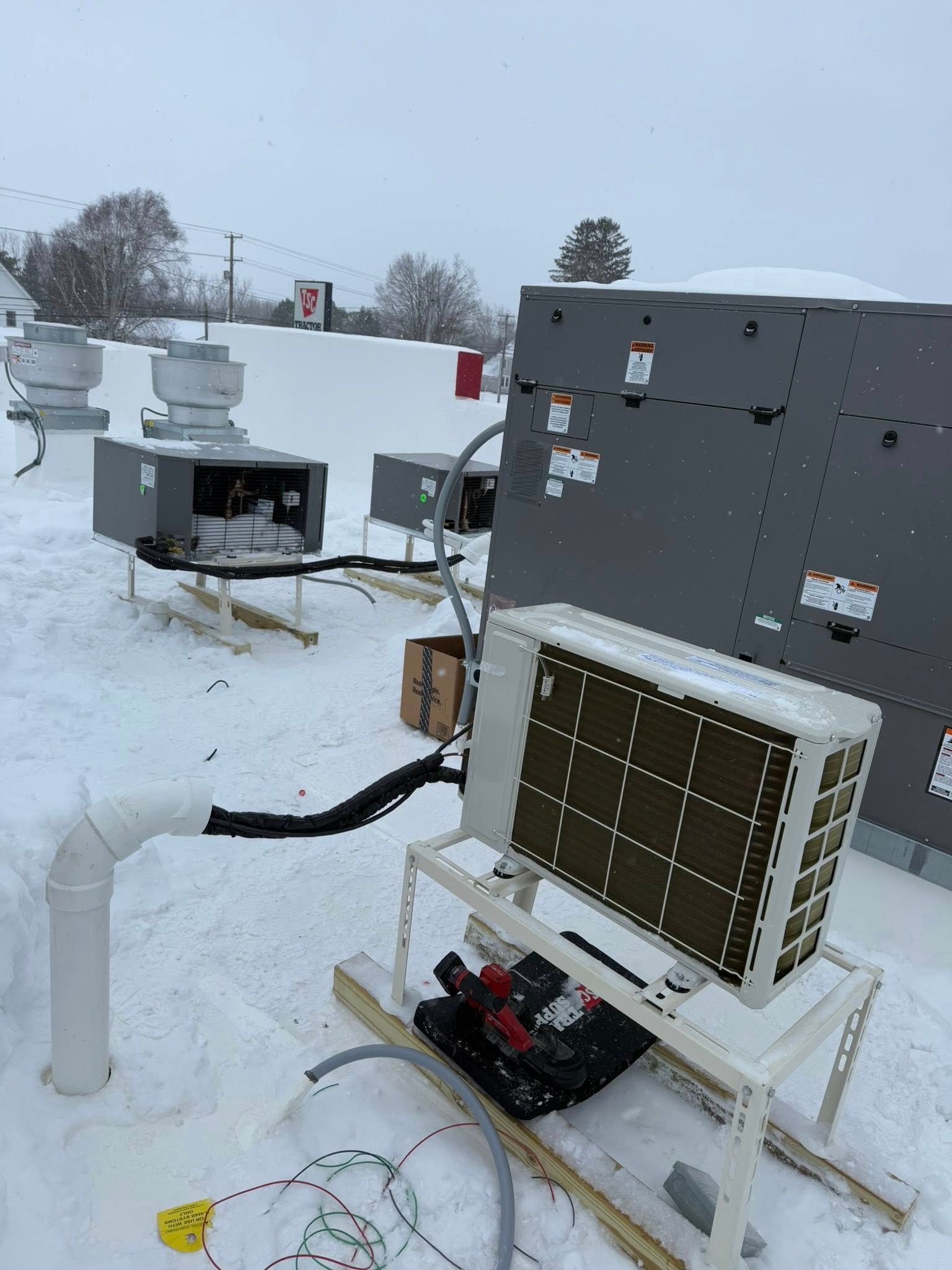 Outdoor HVAC units on a snowy rooftop, including a wall-mounted unit and a small external condenser on a white stand.
