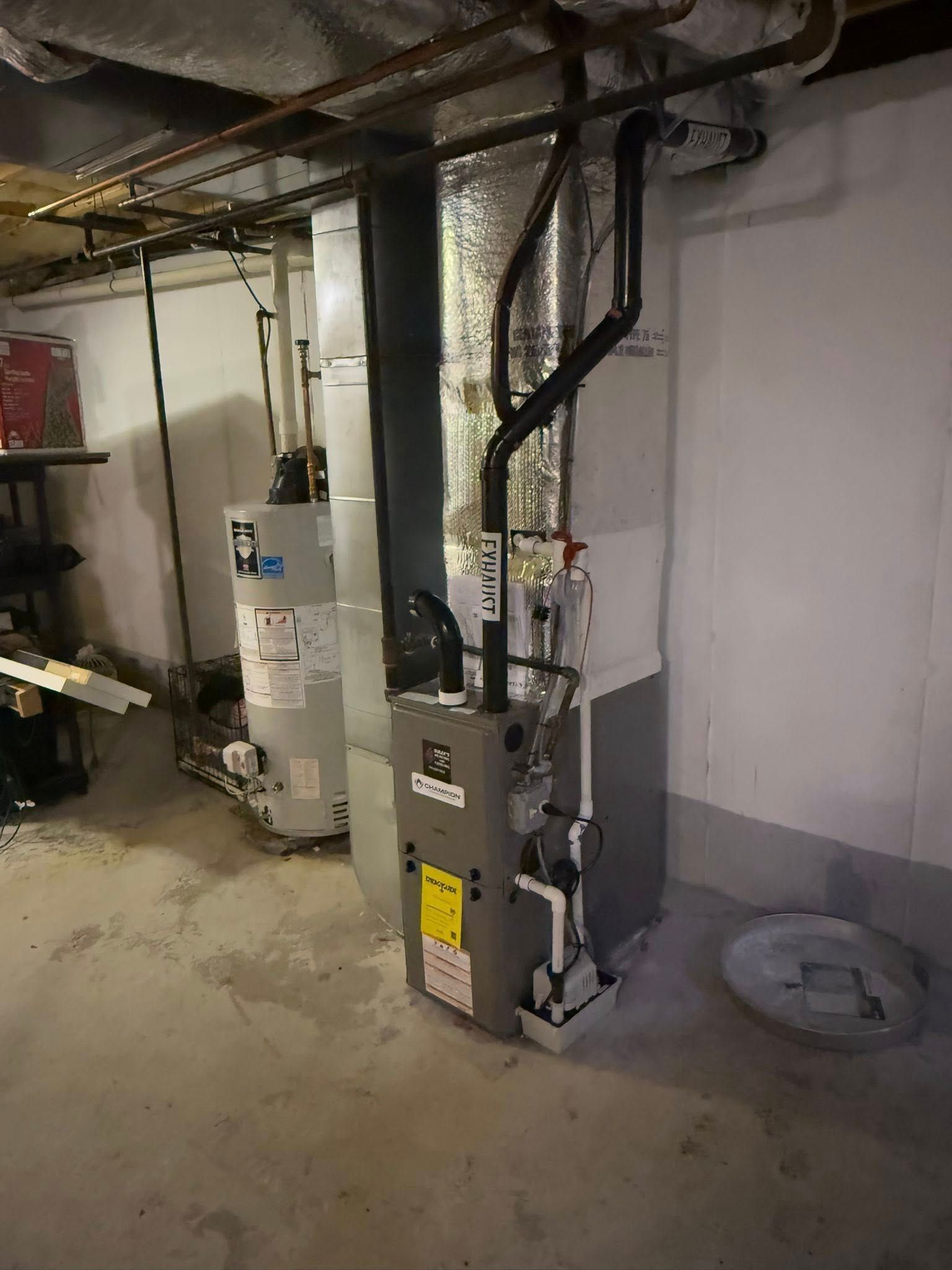 A grey HVAC furnace unit and a water heater stand on a concrete floor in a basement.