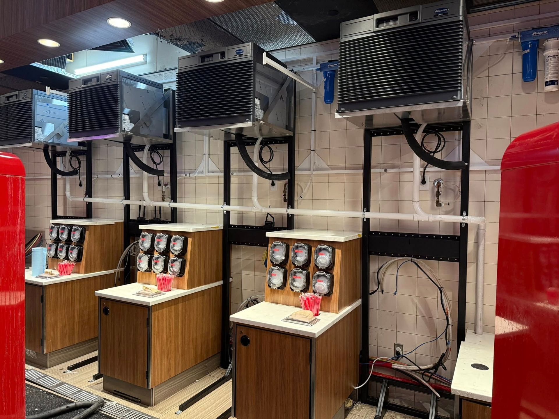 Three soda fountain machines with black air-cooling units mounted on a tiled wall in a service area.