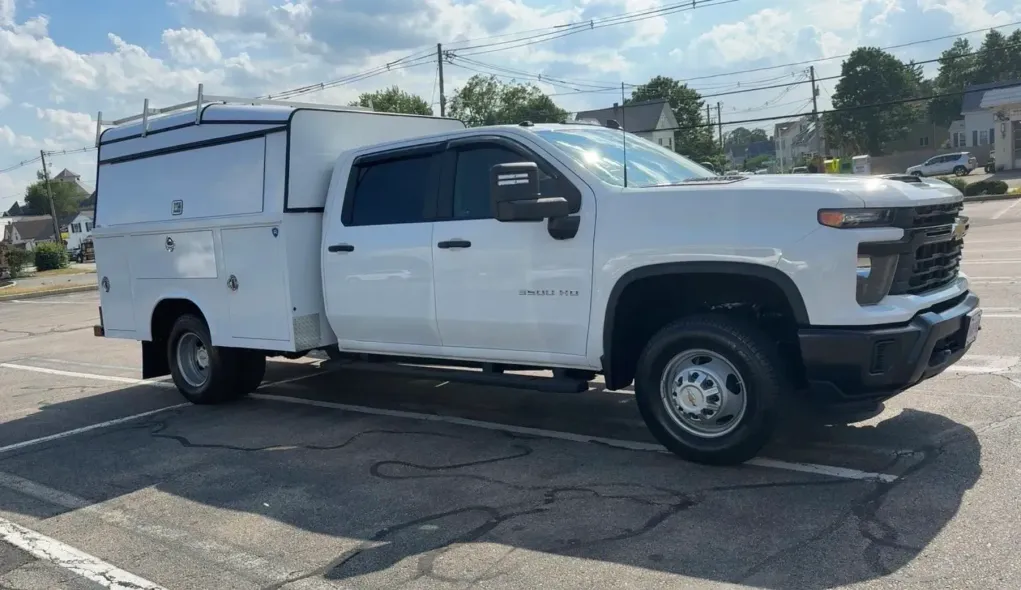 A white Chevrolet Silverado utility truck with a service body parked in an outdoor lot on a sunny day.