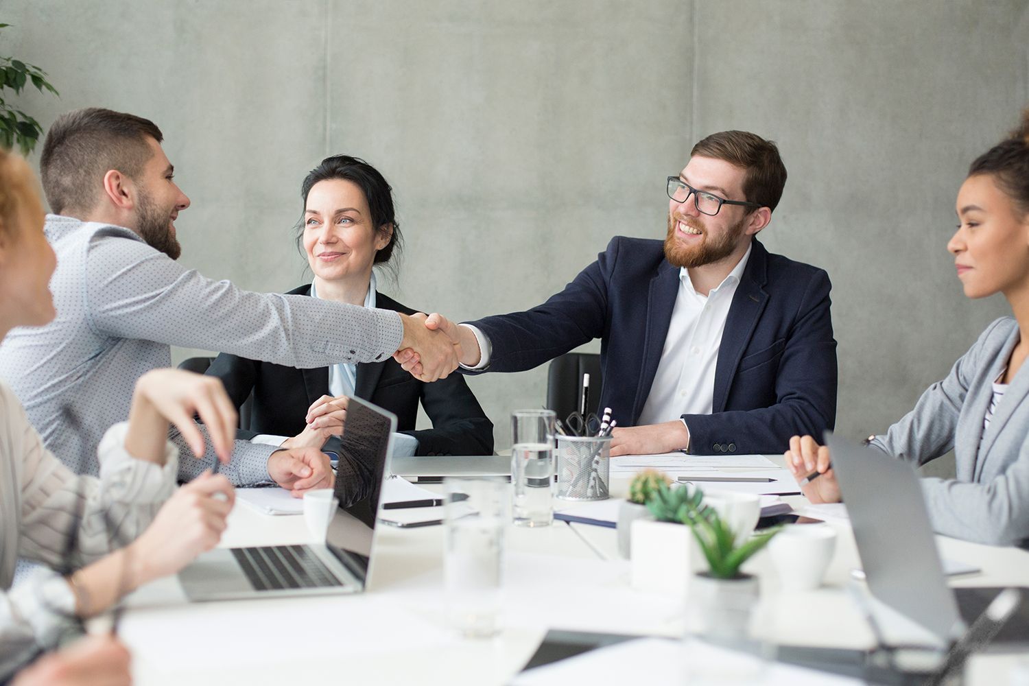 Business meeting with colleagues shaking hands across a conference table, laptops and coffee cups nearby