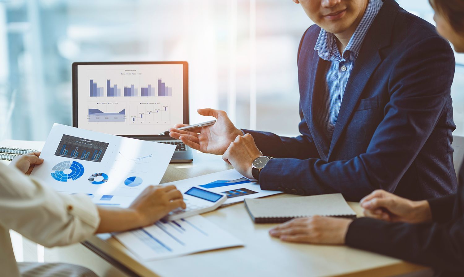 Business meeting with charts on a laptop and documents spread across a table Business meeting with charts on a laptop and documents spread across a table