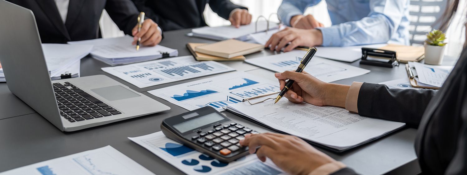 Business meeting with hands reviewing charts, laptop, calculator, and notebooks on a conference table