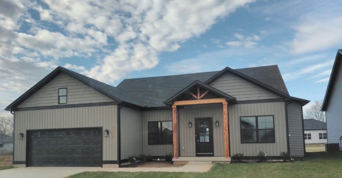Single-story gray house with a dark roof, black garage door, and covered front entry under a cloudy sky