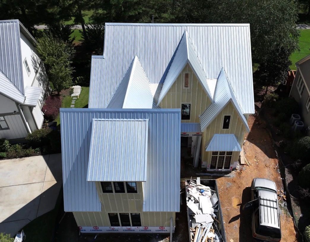 Aerial view of two light-colored houses with metal roofs and a driveway between them.
