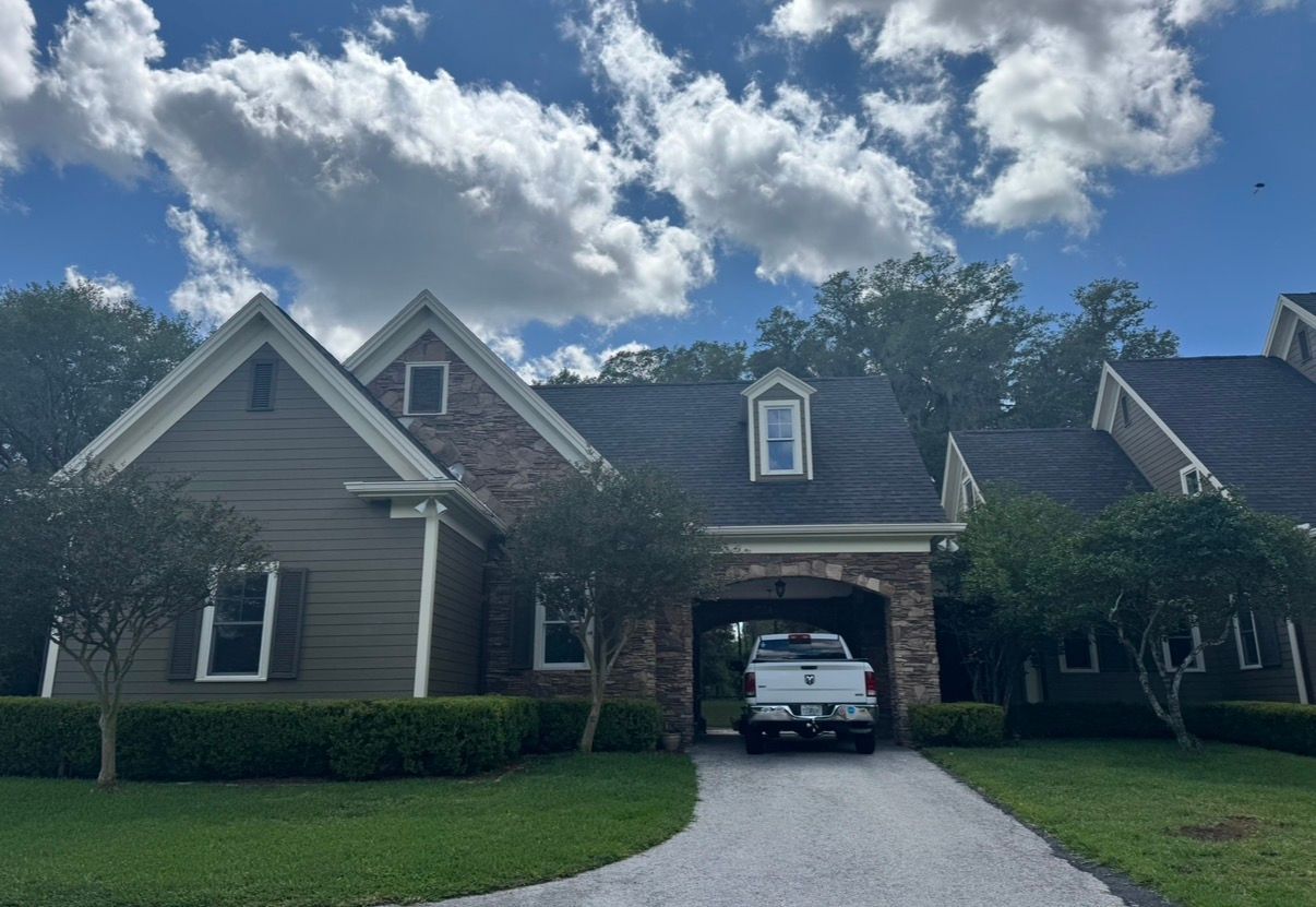 Suburban house with white truck in a carport, gravel driveway, and cloudy sky
