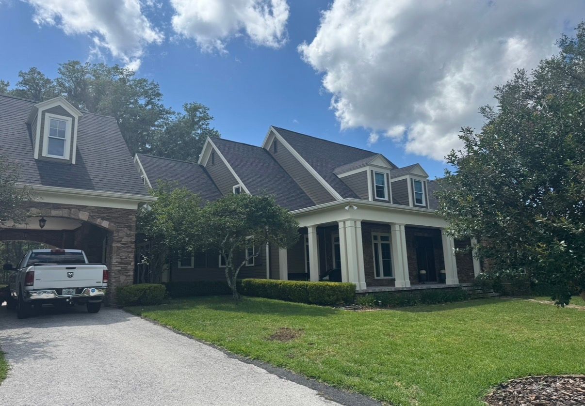 Large suburban house with stone facade, white columns, and a car parked in the driveway under a partly cloudy sky