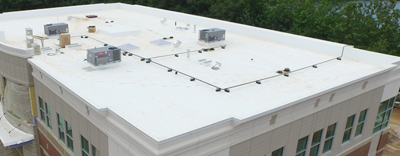 Aerial view of a white flat-roofed building with rooftop equipment and surrounding trees