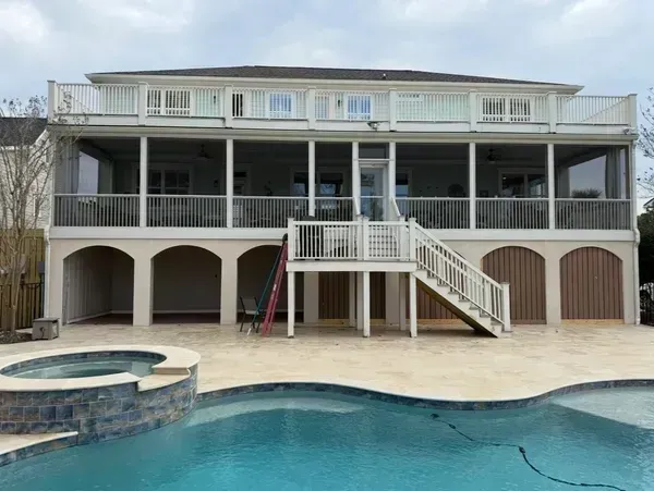 Two-story house with a wraparound deck, stairs, arched lower level, and backyard pool