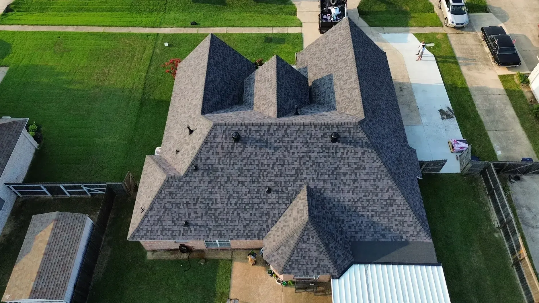Aerial view of a gray-roofed suburban house with green lawns and a driveway.