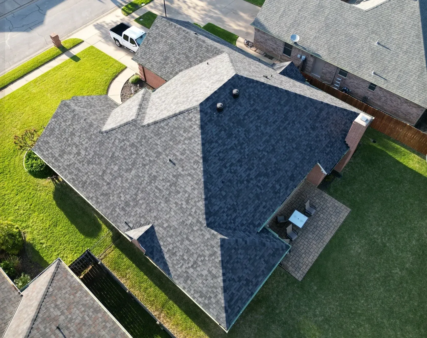 Aerial view of a suburban house with a gray roof and green lawn surrounded by fences.