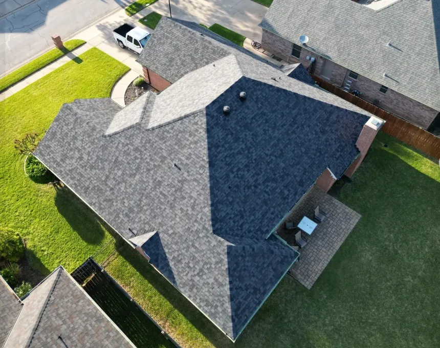 Aerial view of a suburban house with a gray roof and green lawn surrounded by fences.