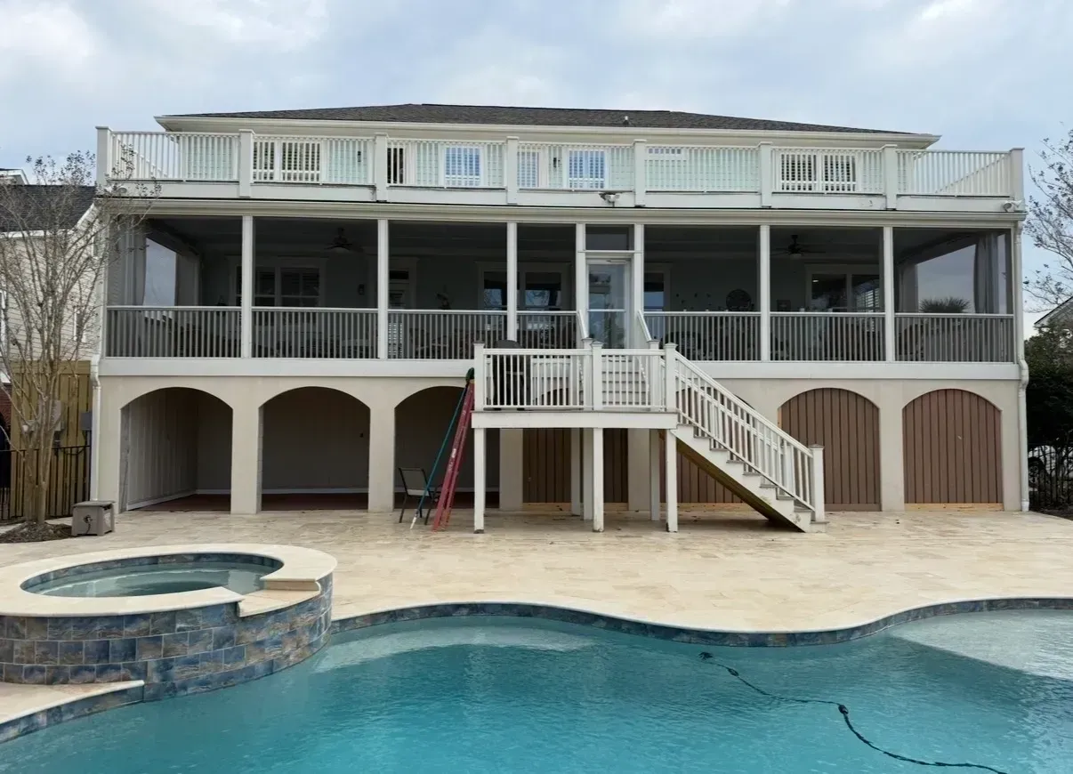 Two-story beach house with white railings and a swimming pool in front