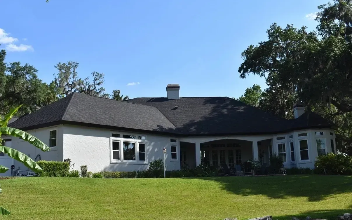 White single-story house with a dark roof and green lawn under a blue sky