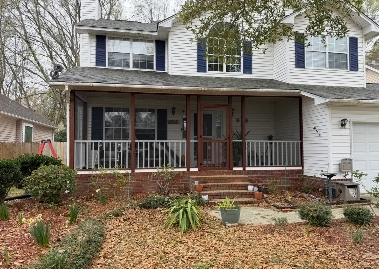 Two-story suburban house with a covered front porch, white siding, and bare winter landscaping