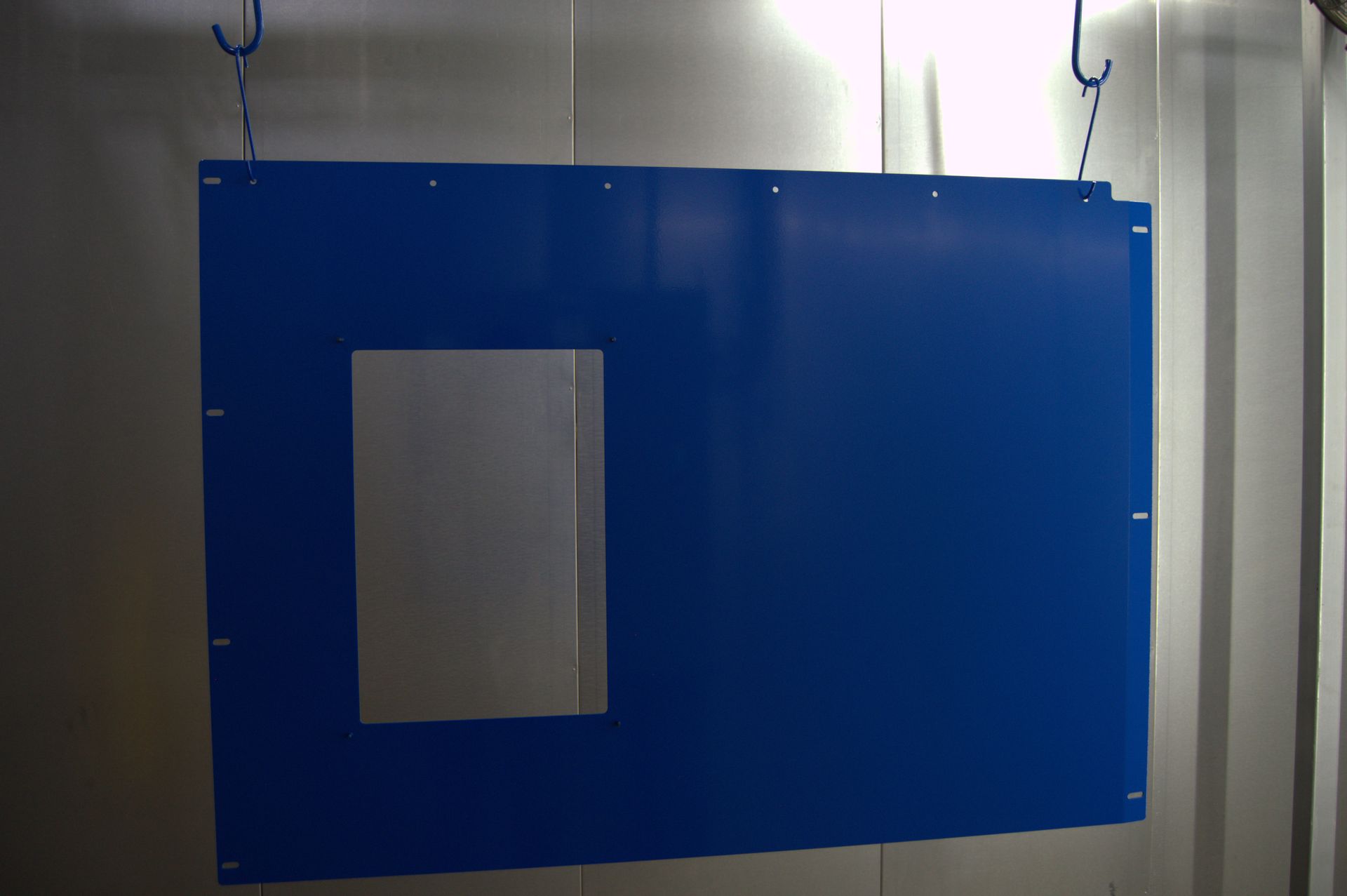 Blue metal panel with a rectangular cutout, hanging in a spray booth.