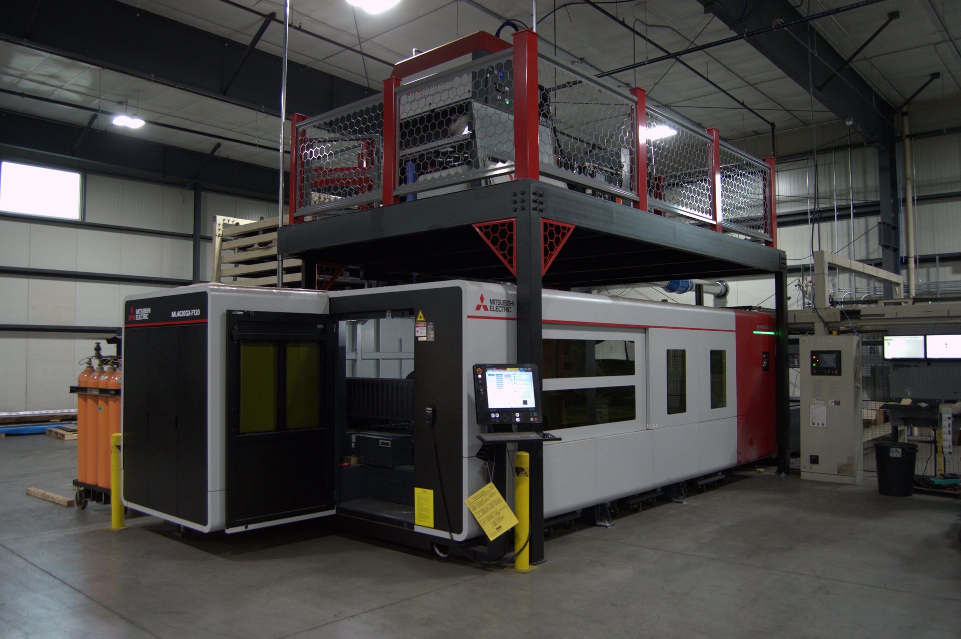 Industrial laser cutting machine in a factory setting with a protective mezzanine above.