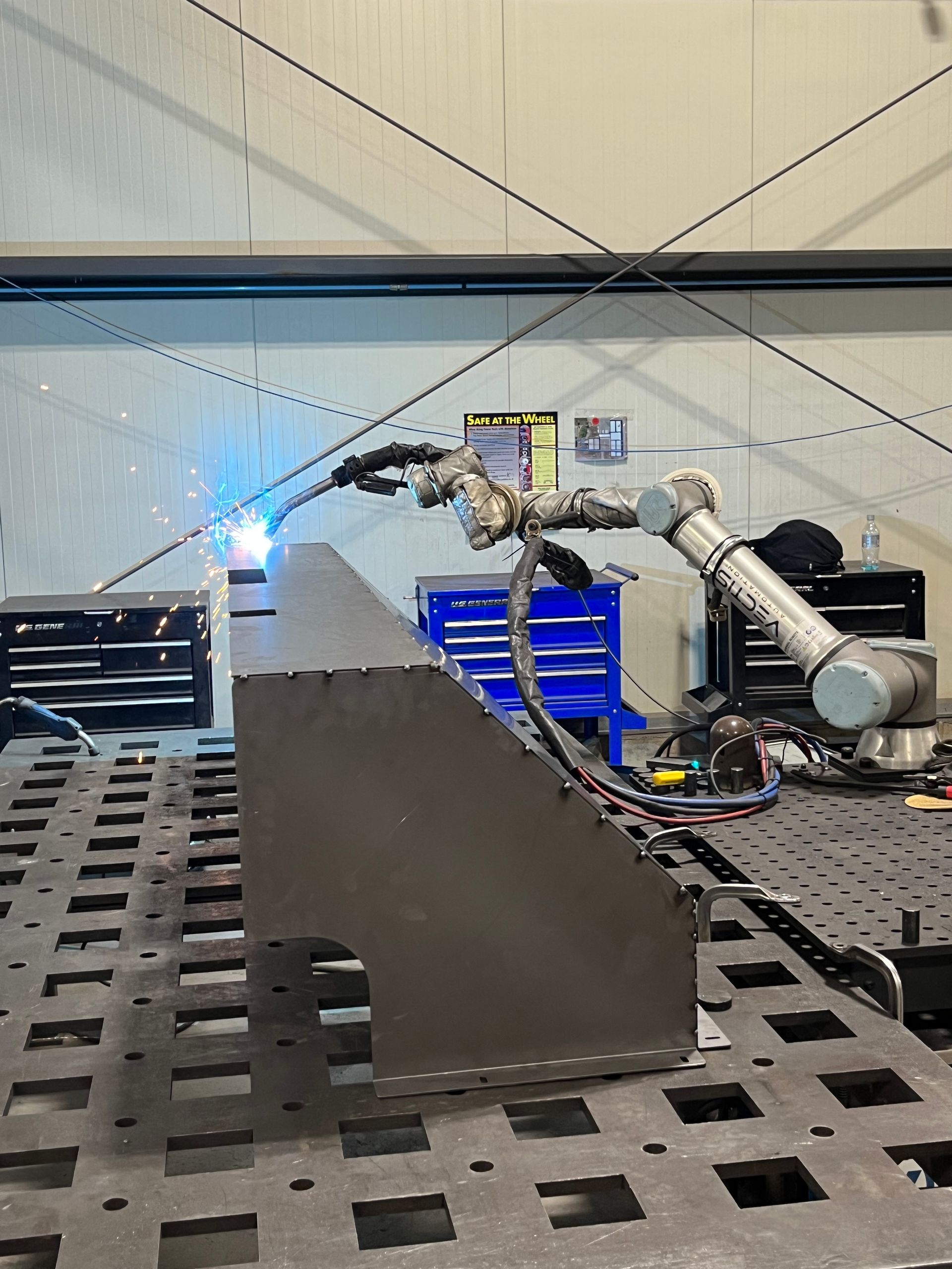 A robotic arm is welding a piece of metal on a table.