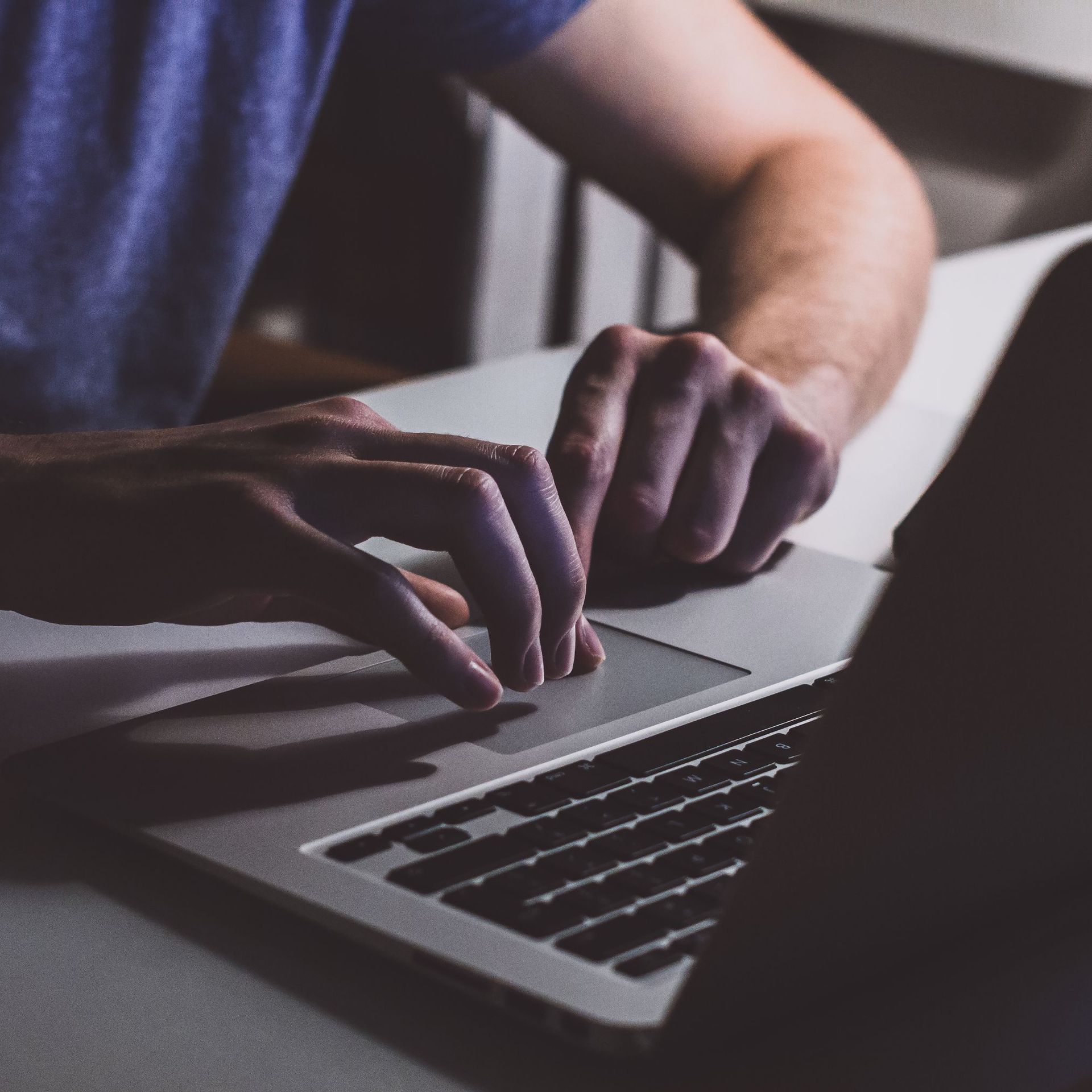 Person's hands using laptop's touchpad, typing. Indoor setting, natural light.