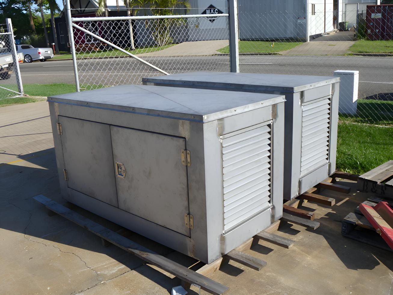 Two Gray Boxes Are Sitting on a Sidewalk Next to a Chain Link Fence — Brian Martin's Sheet Metal In North Mackay, QLD