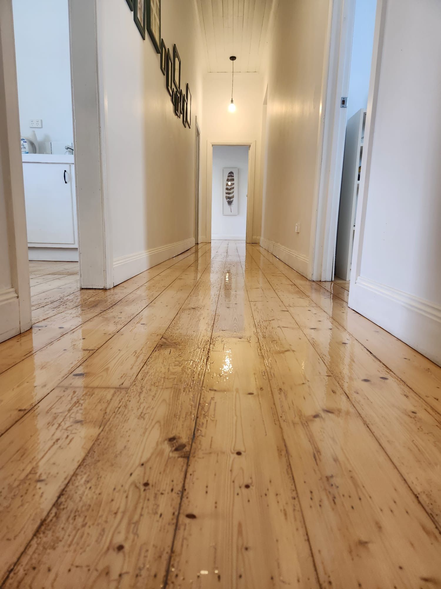 Narrow hallway with glossy wooden floor, white walls, hanging lights, and laundry visible at the far end