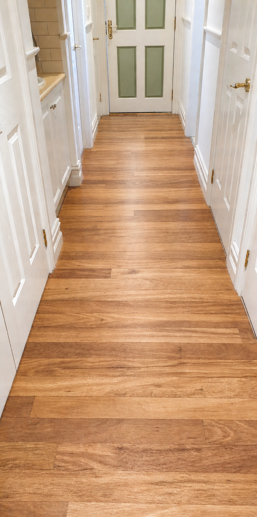 Narrow hallway with hardwood floor, white walls, and a green door at the end