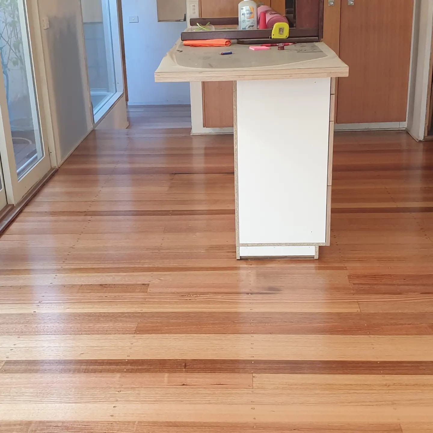 Empty kitchen with a white island and wooden floor, seen from a doorway.