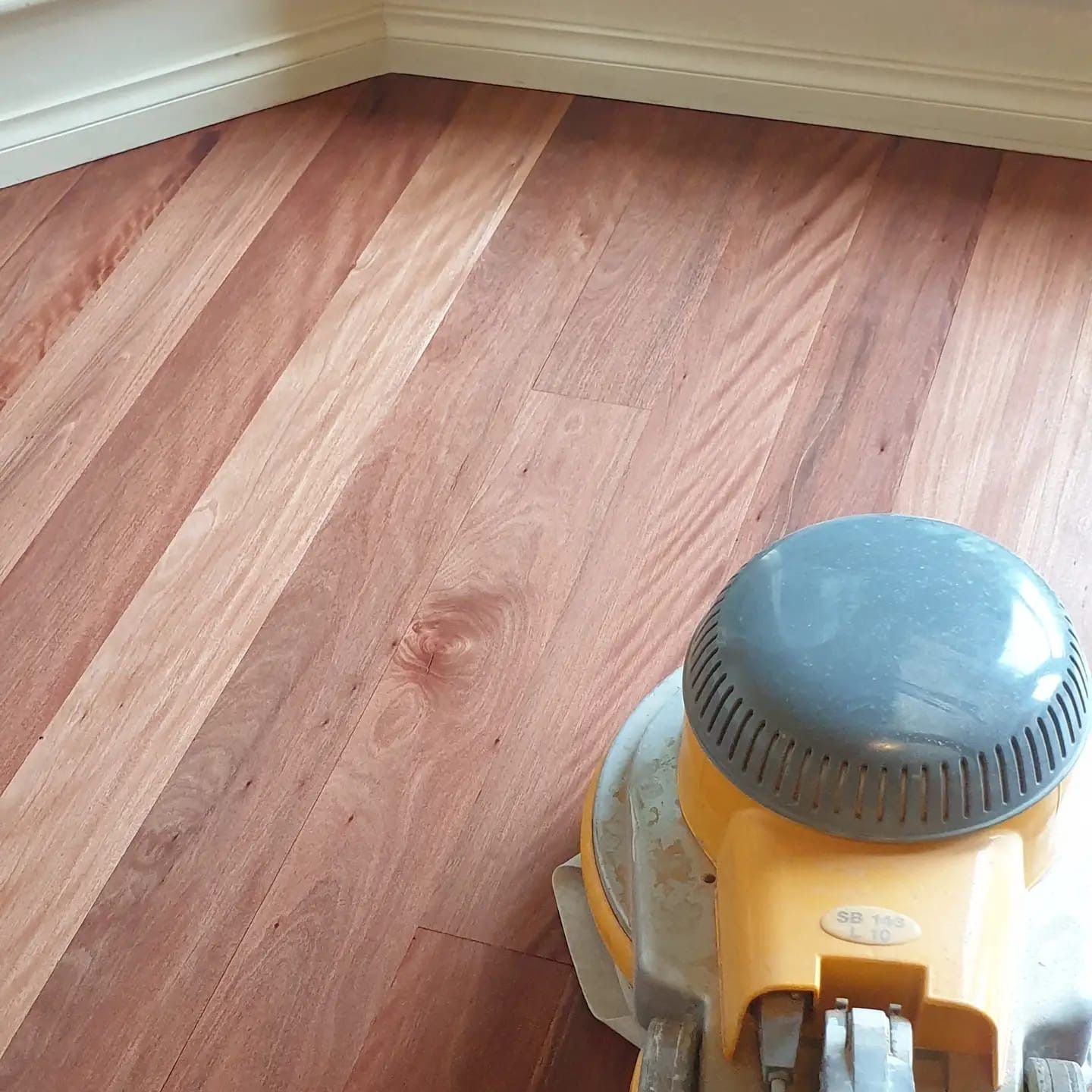 Yellow floor sander on a hardwood floor near a baseboard