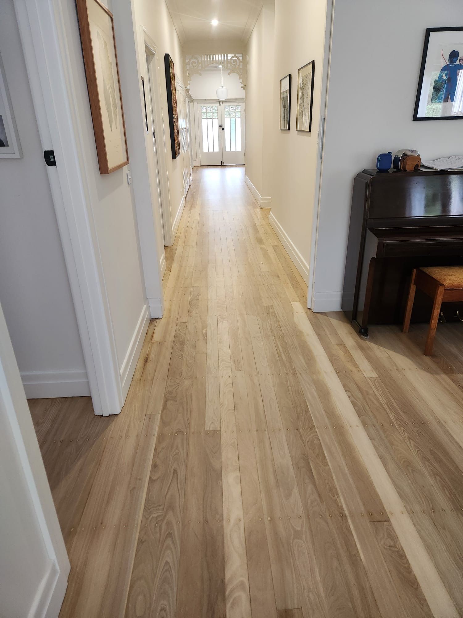 Bright hallway with light wood floors, white walls, and a piano on the right.