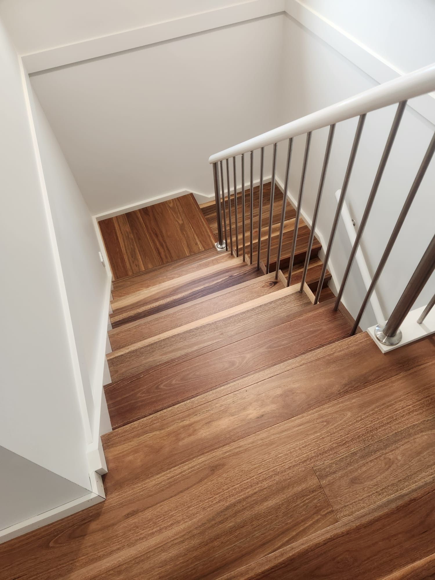 Staircase with wood steps and white walls, viewed from the top with a central handrail.