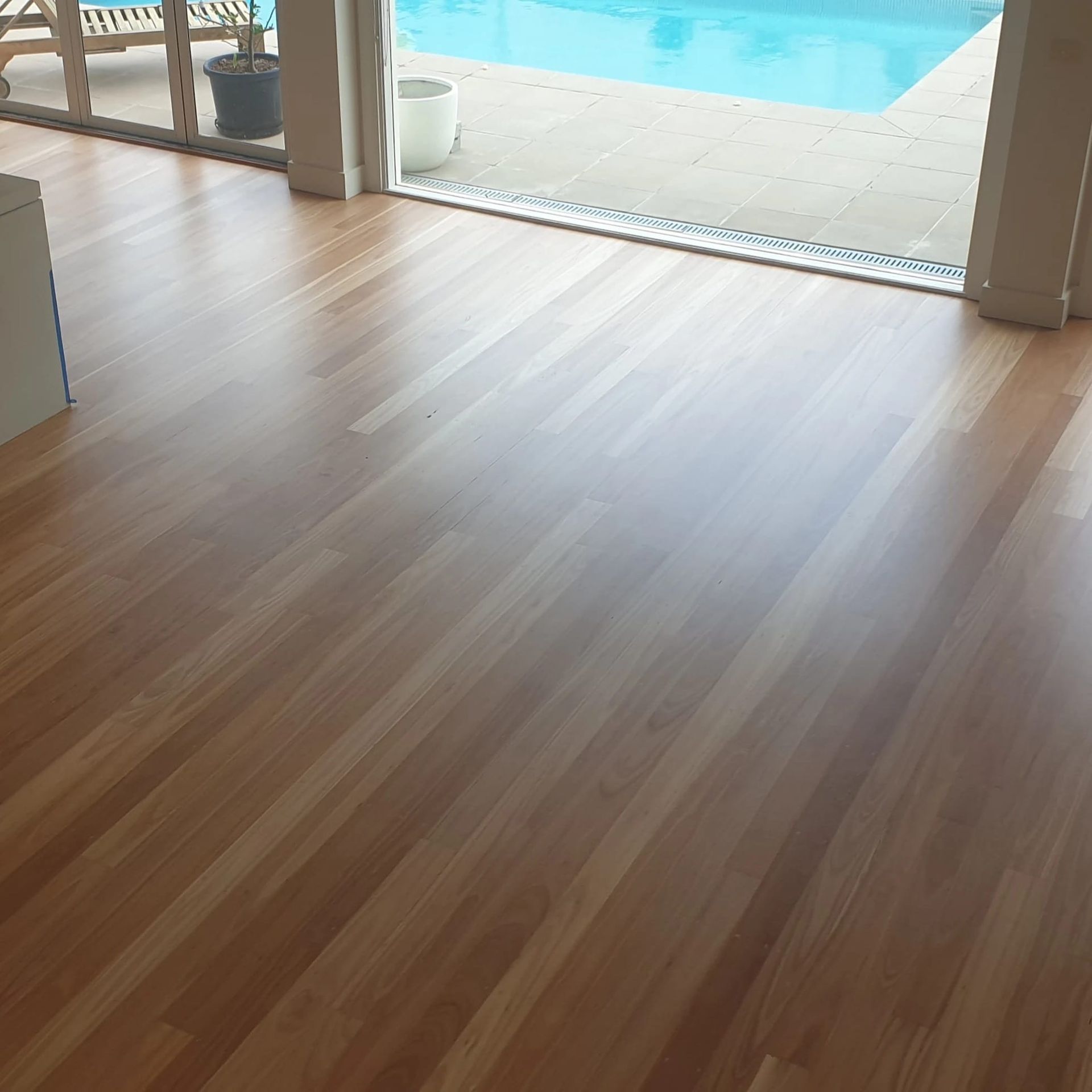Wooden floor overlooking a bright poolside patio through open doors