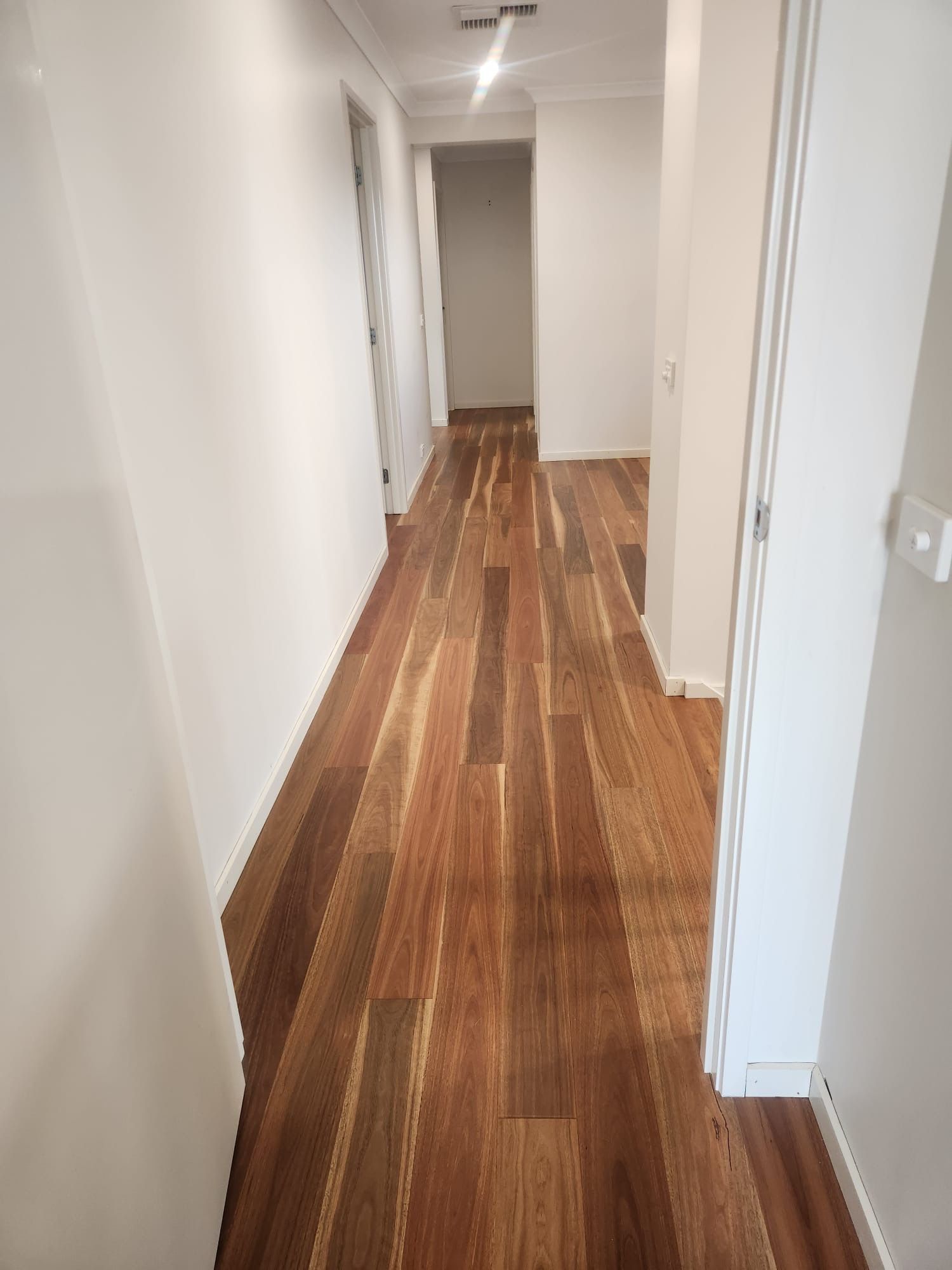 Narrow white hallway with wood-patterned flooring and doors along both sides