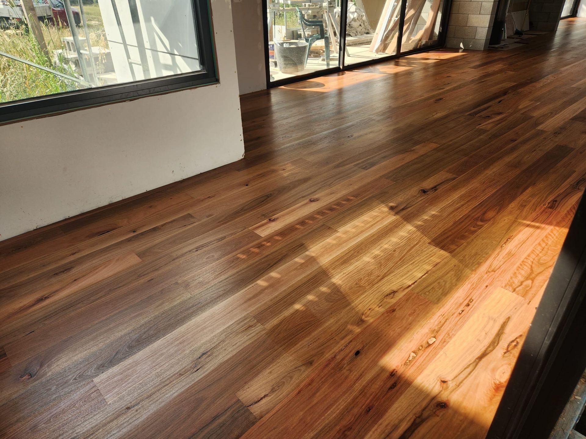 Sunlit hardwood floor in an empty room with large windows