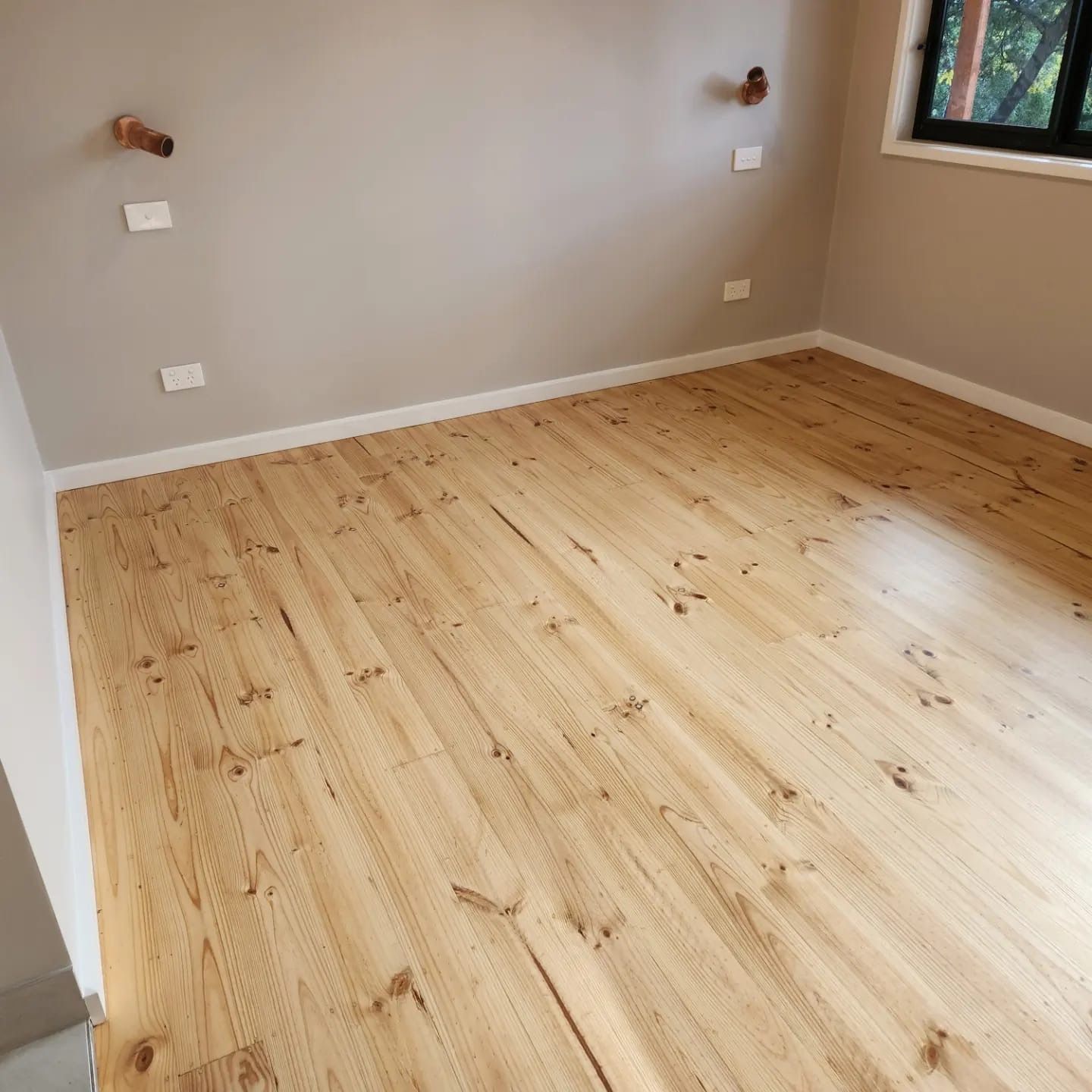 Empty room with light wood flooring, beige walls, white baseboards, and a window.