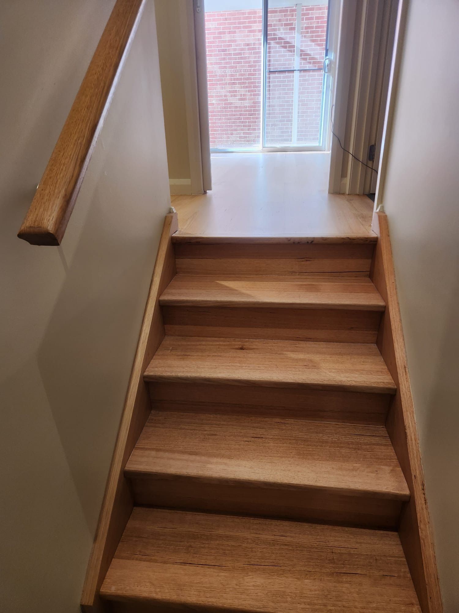 Wooden indoor staircase leading to a bright windowed landing with a handrail on the left.